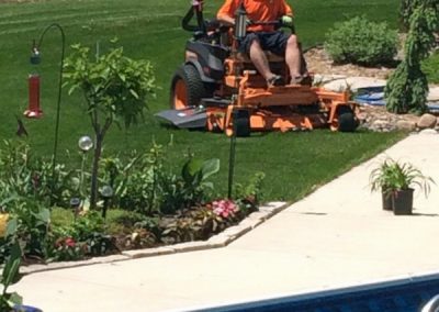 Jeremy Bruce, owner of Midwest Lawn Pro, riding a commercial mower around landscape beds on a residential customer's lawn.