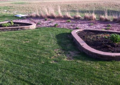 A customer lawn with two raised landscape beds with paver borders.